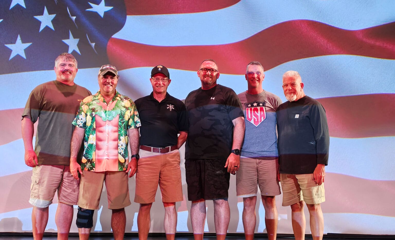 Six men posing before large American flag backdrop