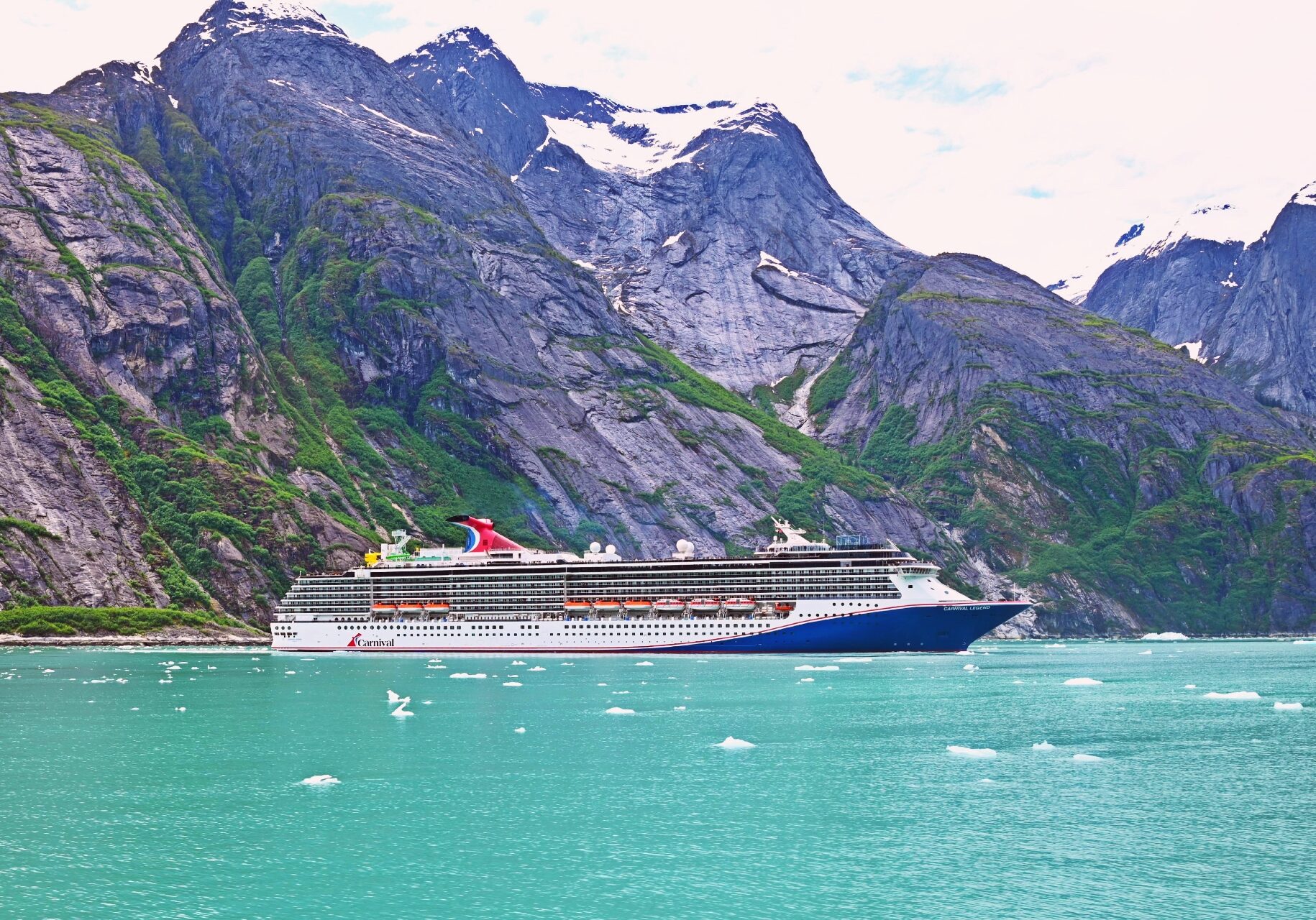 Cruise ship sailing through turquoise glacial fjord mountains