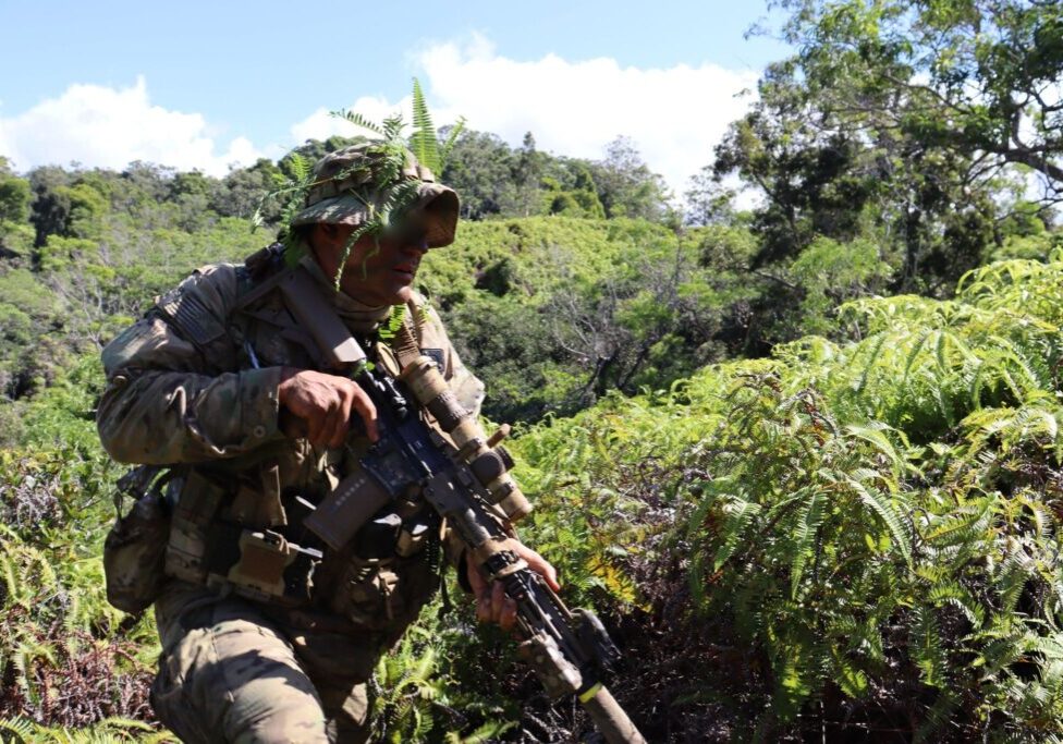 Soldier with rifle moving through dense jungle foliage
